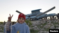 A girl flashes a victory sign as she poses near a helicopter that belongs to forces loyal to Syria's President Bashar Al-Assad after it crashed in Jabal al-Zawiya in the southern countryside of Idlib March 22, 2015.