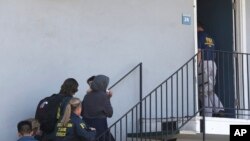 Seorang perempuan menggendong anak sedang dikawal oleh para petugas ke sebuah apartemen menyusul penanggapan pengungsi Irak berusia 45 tahun, Rabu, 15 Agustus, di Sacramento, California.
