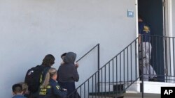 A woman carrying a child is escorted by authorities to an apartment following the arrest of a 45-year-old Iraqi refugee, Omar Ameen, Wednesday, Aug. 15, 2018, in Sacramento, Calif. 