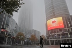 FILE - A man stands near a propaganda display of the Chinese Communist Party (CCP) in the Sanlitun shopping district on a polluted day, in Beijing, China, Nov. 6, 2021.