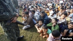 A Thai soldier stands guard as refugees from Burma sit at the Thai-Burma border town of Mae Sot, waiting to go to refugee camps in Thailand, November 9, 2010.