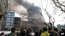 Iranians watch the Plasco building, with smoke rising from its windows, in central Tehran, Iran, Jan. 19, 2017. The high-rise building engulfed by a fire collapsed Thursday as scores of firefighters battled the blaze.