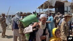 Pakistani soldiers stand guard while stranded people walk towards the Afghan side at a border crossing point, in Chaman, Pakistan, Aug. 13, 2021. 