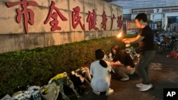 A woman lights a candle near flowers placed outside the Zhuhai People's Fitness Plaza where a man deliberately rammed his car into people exercising at the sports center, in Zhuhai in southern China's Guangdong province, Nov. 12, 2024.