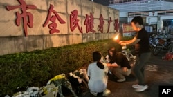 A woman lights a candle near flowers placed outside the Zhuhai People's Fitness Plaza where a man deliberately rammed his car into people exercising at the sports center, in Zhuhai in southern China's Guangdong province, Nov. 12, 2024.