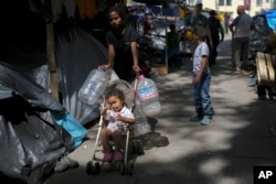 A Central American youth carries plastic containers as she goes to fetch water at a migrant tent encampment set up on the plaza of the Santa Cruz y La Soledad Catholic parish church, in La Merced neighborhood of Mexico City, July 8, 2024.