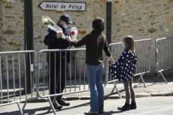 A woman hands flowers to an officer to be taken to the police station where a female police worker was stabbed to death two days earlier, in Rambouillet, southwest of Paris, France, April 25, 2021.