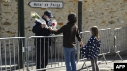 A woman hands flowers to an officer to be taken to the police station where a female police worker was stabbed to death two days earlier, in Rambouillet, southwest of Paris, France, April 25, 2021. 