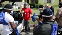 Morris Copeland, of the Strategic Urban Response to Guideline Education group, center, passes out kits to be distributed to residents in COVID-19 hot spots, July 1, 2020, in the Liberty City neighborhood of Miami.