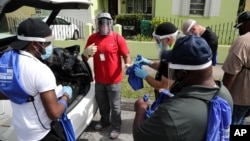 Morris Copeland, of the Strategic Urban Response to Guideline Education group, center, passes out kits to be distributed to residents in COVID-19 hot spots, July 1, 2020, in the Liberty City neighborhood of Miami.