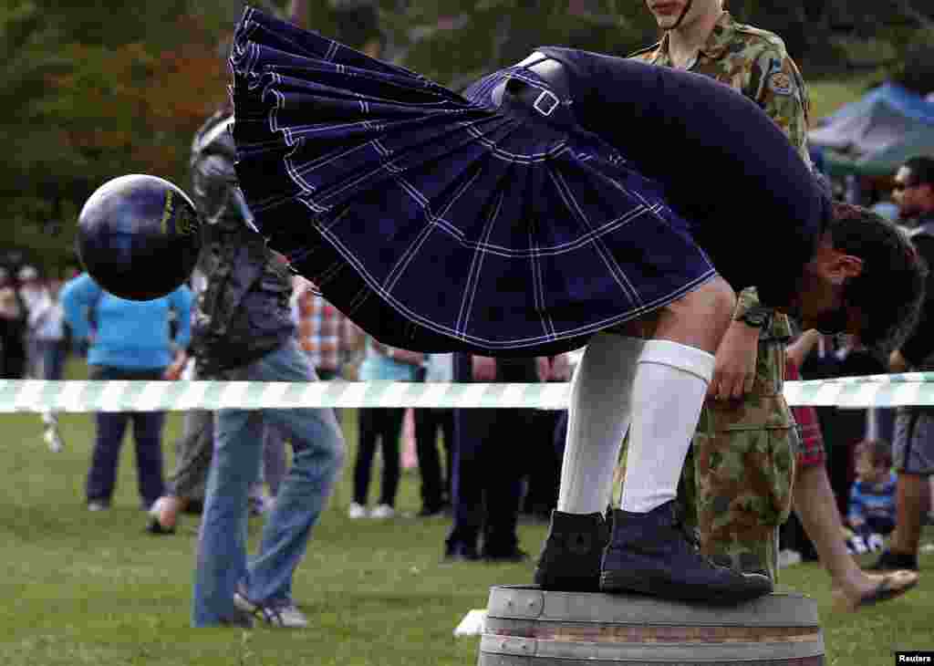 Seorang lawan mengenakan kilt dan berdiri di sebuah tong melemparkan bola di antar kedua kakinya dalam kontes &#39;brigaball&#39; pada ke-36 Bundanoon Highland Gathering yang diadakan di Southern Highlands of New South Wales, Australia, 6 April 2013. 