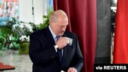 Belarusian President Alexander Lukashenko holds a ballot and a passport before casting his vote at a polling station during the presidential election in Minsk, Belarus, Aug. 9, 2020. 