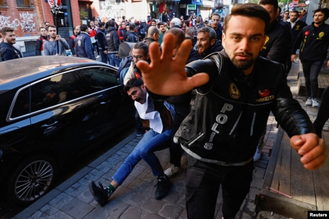 A police officer gestures towards camera as they detain a demonstrator during a protest to defy a ban and march on Taksim Square to celebrate May Day in Istanbul, Turkey May 1, 2023. (REUTERS/Kemal Aslan)