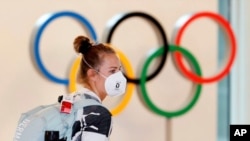 Un atleta alemana, con mascarilla, pasa junto a la exhibición de anillos olímpicos a su llegada al aeropuerto de Haneda en Tokio, el 1 de julio de 2021.