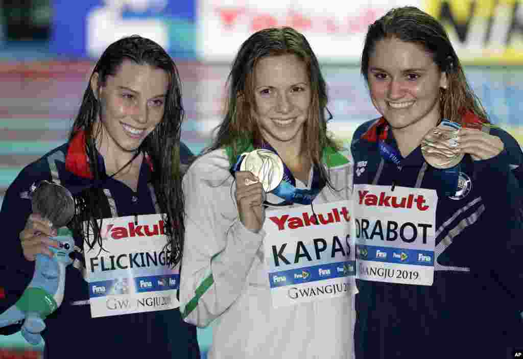 هالی فلیکنگر (چپ) و کتی درابوت (راست) دو شناگر آمریکایی به همراه شناگر مجارستانی روی سکوی قهرمانی ۲۰۰ متر پروانه در مسابقات جهانی قهرمانی شنا در کره جنوبی.&nbsp;