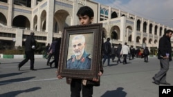 Seorang anak lelaki membawa potret Pengawal Revolusi Iran Jenderal Qassem Soleimani, yang terbunuh dalam serangan udara AS di Irak, sebelum salat Jumat di Teheran, Iran, Jumat 3 Januari 2020. (Foto: AP)