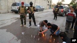 Pasukan keamanan berjaga-jaga sementara para jurnalis Irak menyalakan lilin di tempat kepala biro Radio Free Iraq di Baghdad, Irak (22/3). (AP/Karim Kadim)