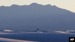 FILE - Visitors walk on sand dunes as the sun sets, March 5, 2015, in White Sands National Monument, New Mexico.