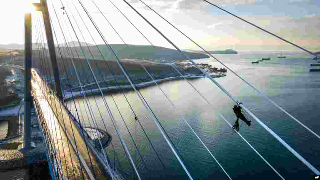 Seorang petugas membersihkan lapisan es dari kabel-kabel baja di Jembatan Russky yang melintasi Selat Bosphorus Timur di Vladivostok, Rusia, Senin, 30 November 2020. (Foto: AP)&nbsp;