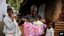 Veronica Atieno, kiri, melihat suaminya Gabriel Owour Juma menggendong putri mereka Shaniz Joy Juma, yang dilahirkan sebulan sebelumnya oleh dukun bayi tradisional. (Foto: AP)