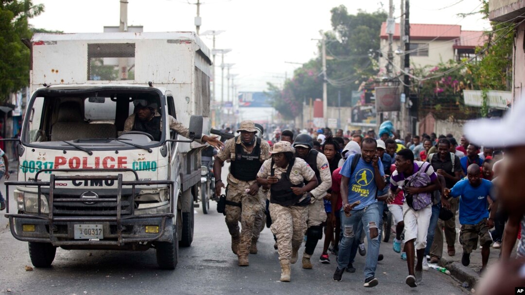 Petugas kepolisian dan demonstran berlindung dibalik truk polisi saat unjuk rasa menuntut pengunduran diri Presiden Jovenel Moise, di Port-au-Prince, Haiti, 18 November 2019. 