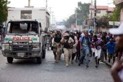 Police officers and protesters take cover behind a police truck as shots ring out during a protest to demand the resignation of Haiti's president Jovenel Moise in Port-au-Prince, Haiti, Nov. 18, 2019.