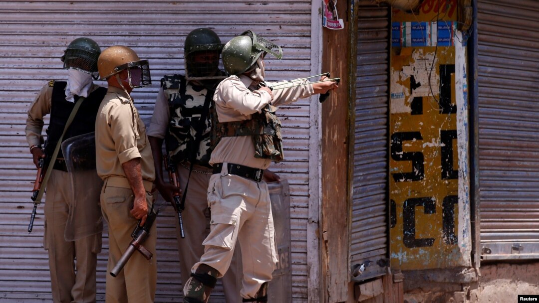 Seorang polisi India menggunakan ketapel untuk melemparkan batu ke arah para pemrotes saat terjadi bentrokan pada peringatan pembunuhan pasukan India Burhan Wani, komandan kelompok militan Hizbul Mujahidin, di pusat kota Srinagar, 8 Juli 2017.