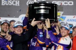 Denny Hamlin, right, celebrates as he and crew members hoist the championship trophy after winning the NASCAR Daytona 500 auto race at Daytona International Speedway, Feb. 17, 2020, in Daytona Beach, Fla.