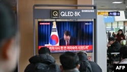 La gente mira una transmisión televisiva en vivo del presidente de Corea del Sur, Yoon Suk Yeol, haciendo una reverencia después del final de su discurso a la nación, en una estación de tren en Seúl, el 7 de diciembre de 2024.