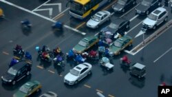 FILE - People on electric bikes cross a busy traffic intersection on a rainy day on Chang'an Avenue in Beijing, China.