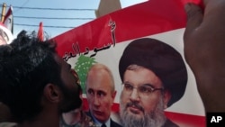 FILE - A Syrian who lives in Lebanon kisses a poster with photos of Russian President Vladimir Putin (C) and Hezbollah leader Sheikh Hassan Nasrallah, during a rally to thank Moscow for its intervention in Syria, in front of the Russian embassy in Lebanon, Oct. 18, 2015.