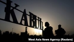 FILE - People stand in front of a sign at the international airport in Kabul, Afghanistan, Sept. 9, 2021. 