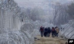 FILE - Refugees and migrants, who entered Macedonia from Greece illegally, walk between the two lines of the protective fence along the border line, near southern Macedonia's town of Gevgelija, Monday, Feb. 29, 2016.