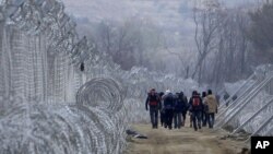 FILE - Refugees and migrants, who entered Macedonia from Greece illegally, walk between the two lines of the protective fence along the border line, near southern Macedonia's town of Gevgelija, Feb. 29, 2016.