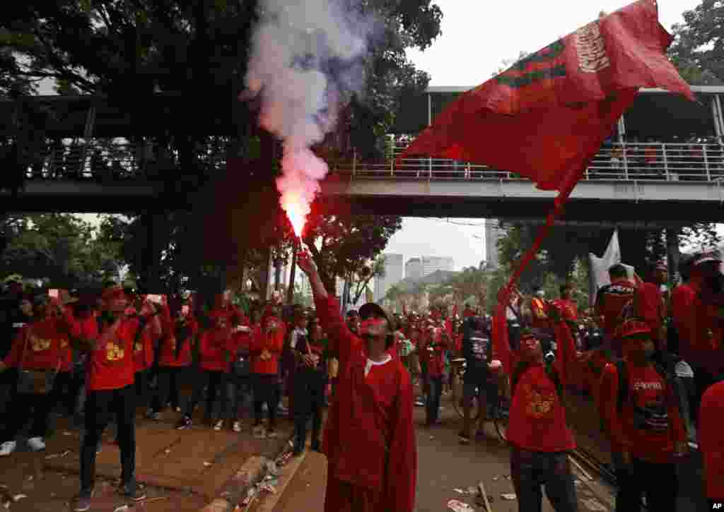 A worker lights up a flare during a May Day rally in Jakarta, Indonesia, Monday, May 1, 2017. 