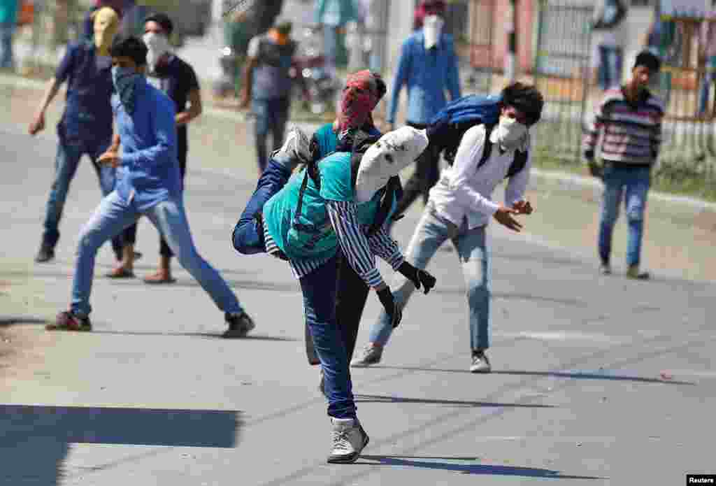 Warga Kashmir yang mengenakan topeng dan masker melakukan protes dengan melempar batu ke arah pasukan keamanan India di ibukota Kashmir-India, Srinagar.