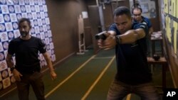 Shooting instructor Alex Cordeiro, right, holds a fake pistol as he demonstrates a movement to Rildo Anjos, owner of the Calibre 12 gun club, during a practice session in Sao Goncalo, Brazil, Jan. 10, 2019.