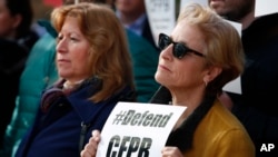 Sally Greenberg, with the National Consumers League, right, holds a sign that says "Defend CFPB" outside of the Consumer Financial Protection Bureau in Washington, Nov. 27, 2017.