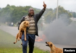 A protester gestures as he holds a dog before a burning barricade during protests in Harare, Zimbabwe, January 15, 2019.