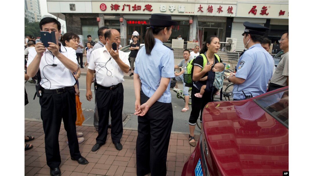 FILE - Yuan Shanshan, third right, the wife of detained Chinese lawyer Xie Yanyi, carries her child as she talks to a police officer while other plain clothes security personnel film journalists near the Tianjin No. 2 Intermediate People's Court in northern China.