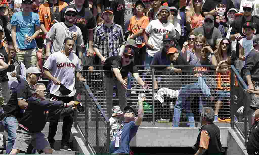 A fan holding a child, bottom, catches Colorado Rockies' Troy Tulowitzki's two-run home run against the San Francisco Giants during the third inning of a baseball game in San Francisco, June 15, 2014. The Rockies won 8-7.