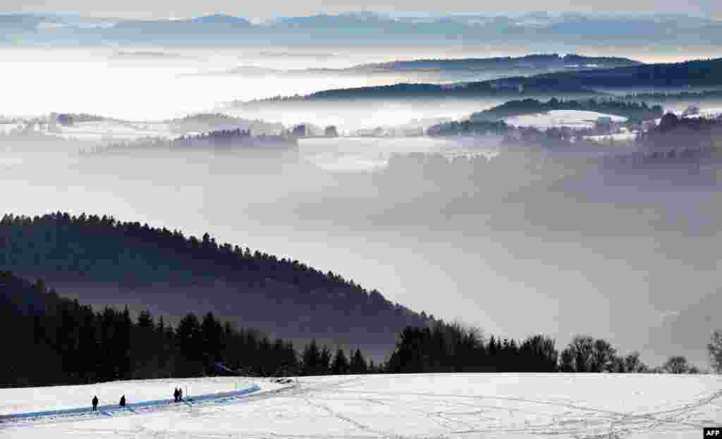 People walk on a snowy landscape as the Swiss Alps are seen in the background and mist partly covers the alpine upland near the southern German town of Höchenschwand. 