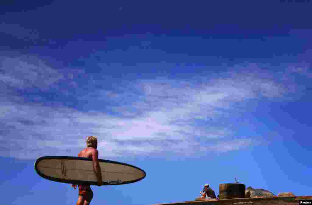 A surfer carrying his board walks towards the beach along a path at Long Reef Beach on a sunny day in Sydney, Australia.