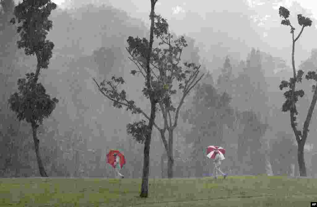 Course marshals carry umbrellas as they make their way toward shelter during a heavy rain at the HSBC Women&#39;s Champions golf tournament at Sentosa Golf Club&#39;s Tanjong course in Singapore.