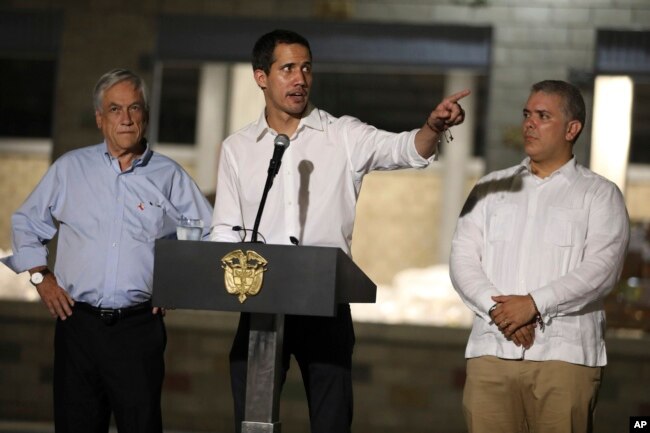 Venezuela's opposition leader Juan Guaido speaks flanked by Chile's President Sebastian Pinera, left, and Colombia's President Ivan Duque in front of a warehouse housing U.S. humanitarian aid destined for Venezuela, in Cucuta, Colombia, Feb. 22, 2019.