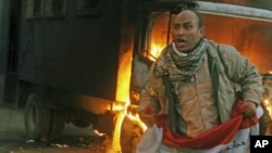 A protester holds an Egyptian flag next to a police vehicle that was set ablaze during clashes between protesters and security forces in Cairo, November 19, 2011.