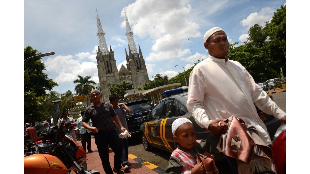 Muslim Indonesia tiba di masjid Istiqlal yang terletak di seberang Katedral Jakarta, terlihat di latar belakang sebagian umat Kristen dan Muslim berada di rumah ibadah mereka masing-masing pada 29 Maret. (Foto: AFP)