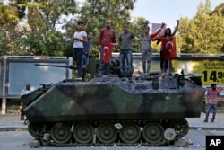 Turkish citizens stand on a damaged Turkish military armored personnel carrier that was attacked by protesters in a street near the Turkish military headquarters in Ankara, July 16, 2016.