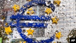 The Euro sculpture in front of the old European Central Bank building is photographed behind rain drops on a window in Frankfurt, Germany, Oct. 18, 2016.