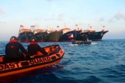 FILE - In this handout photo provided by the Philippine Coast Guard, members of the Philippine Coast Guard use rubber boats as they patrol beside Chinese vessels moored at Whitsun Reef, South China Sea, April 14, 2021.